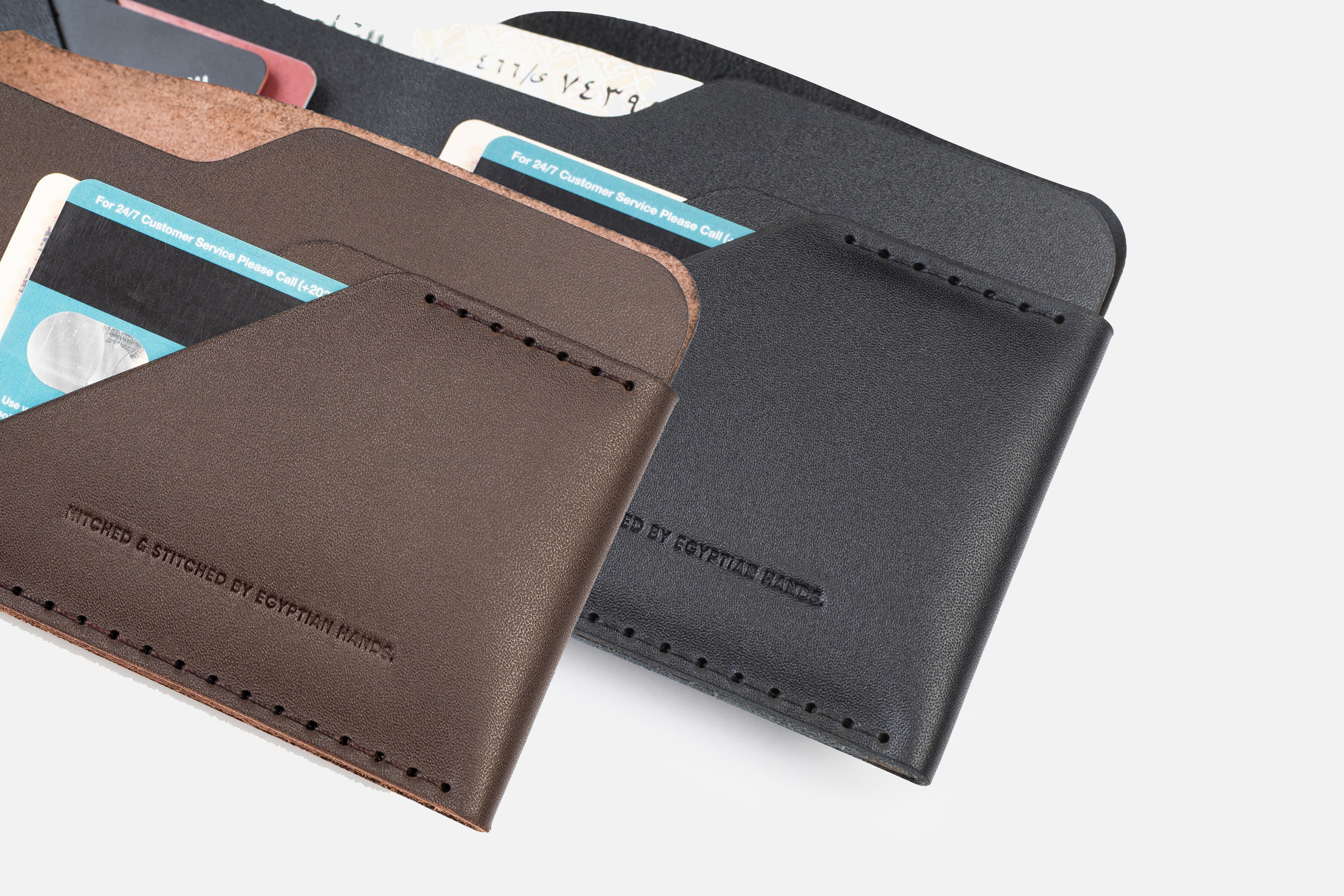 Brown and black leather bifold wallets with credit cards, embossed with Stitched by Egyptian Hands."