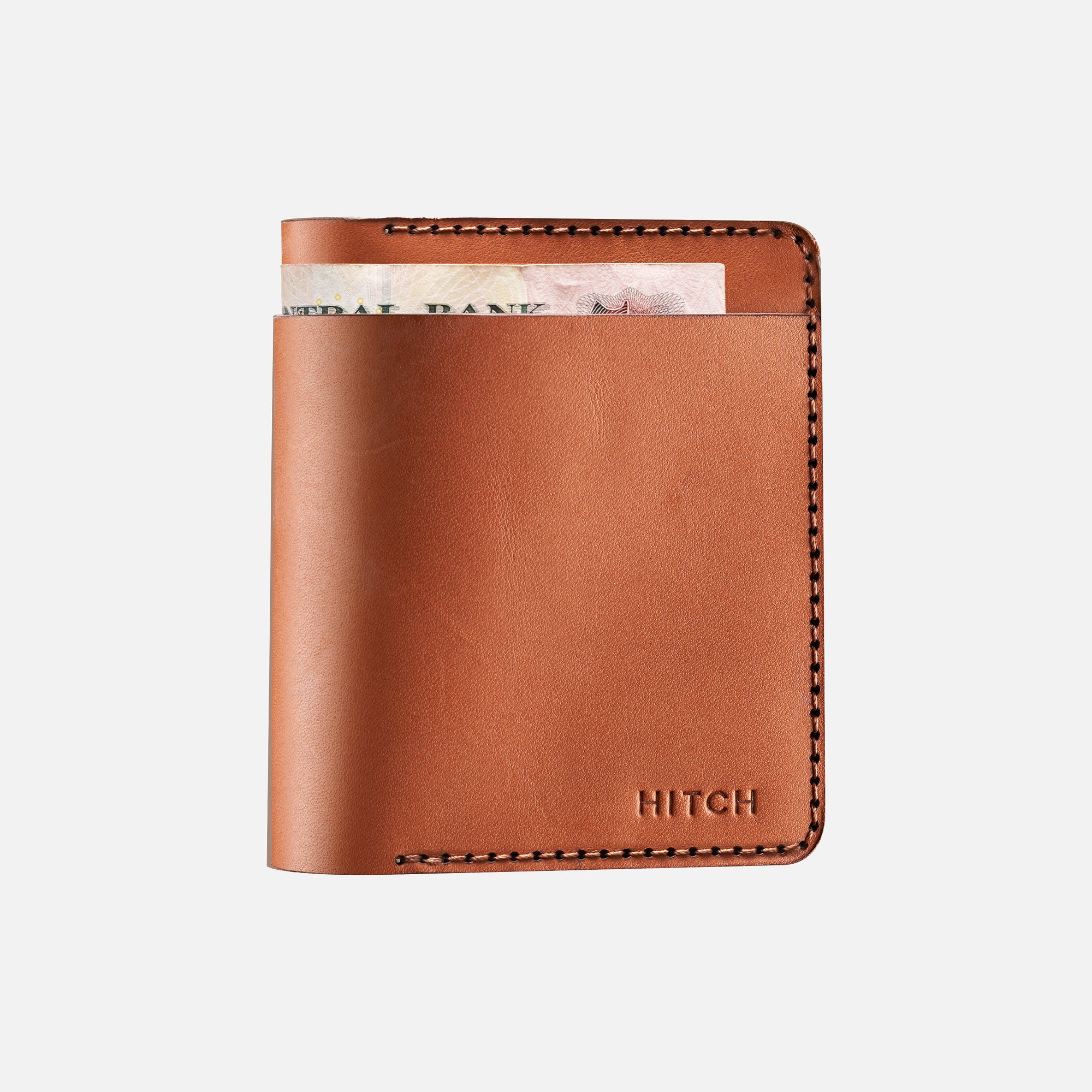 Brown leather bifold wallet with stitched detailing and currency note peeking out, isolated on white background.