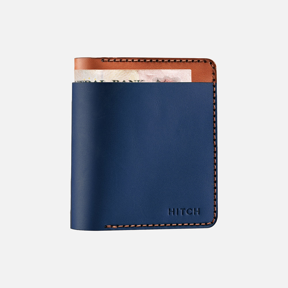 Blue and brown leather bifold wallet with cash peeking out on white background.
