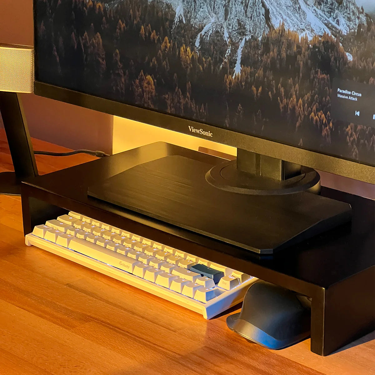Modern stand riser by woodsy with a monitor, mechanical keyboard, mouse on wooden desk and warm lighting.