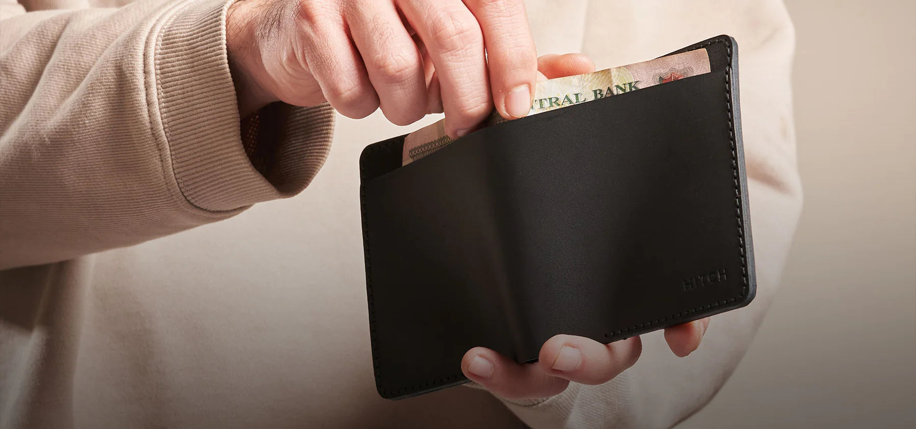 Person pulling cash from a genuine leather wallet in black, minimalist and sleek leather design by "HITCH"
