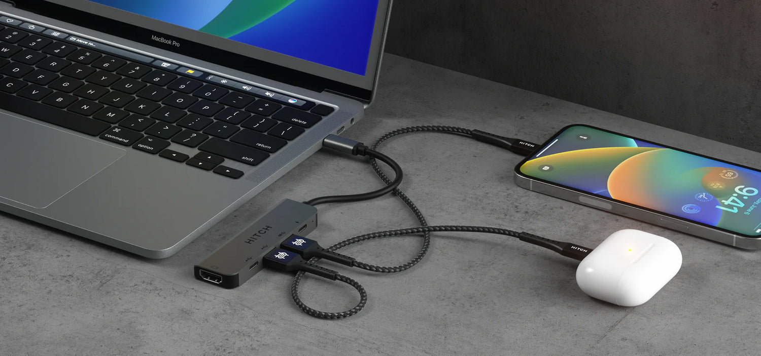 Laptop connected to multi-port adapter with "HITCH" fast charging cables to smartphone and wireless earbuds on desk.