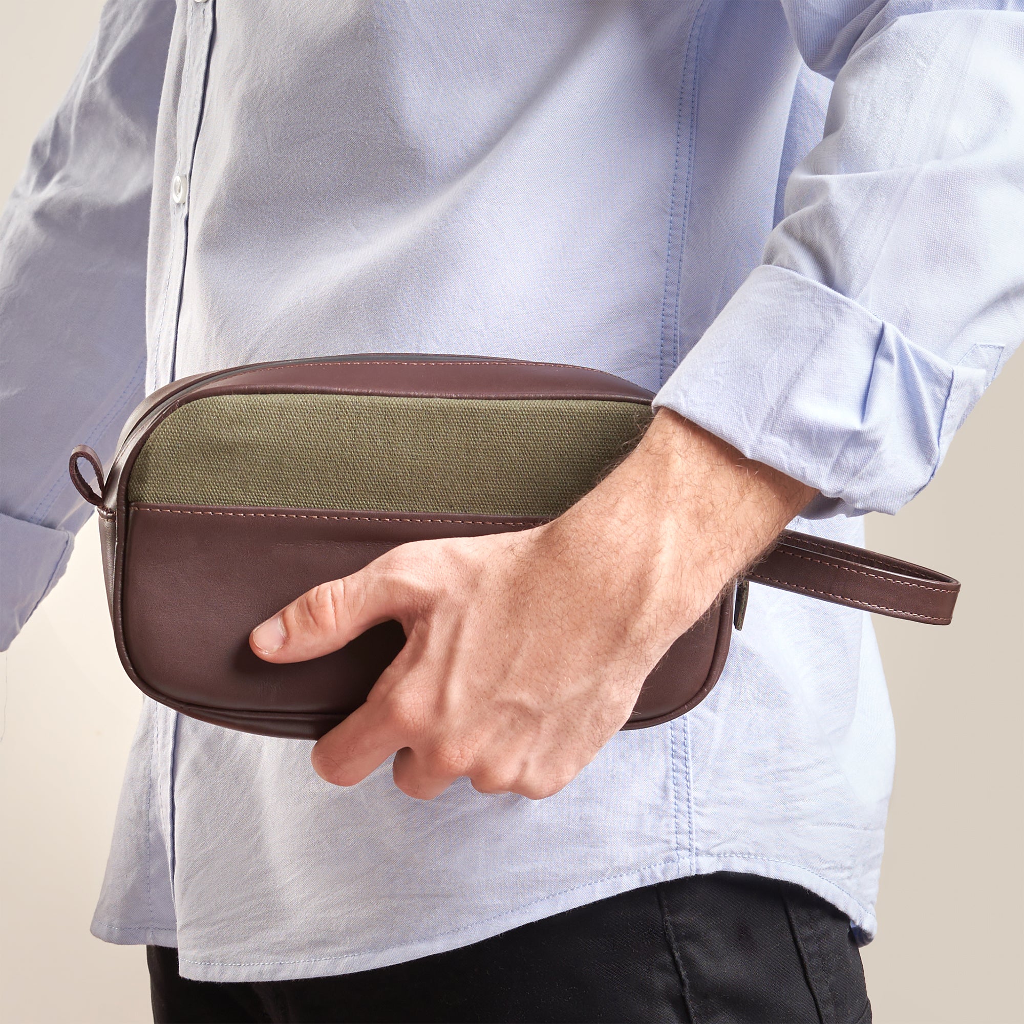 "Man wearing a stylish brown dopp kit with wrist strap over a light blue shirt"