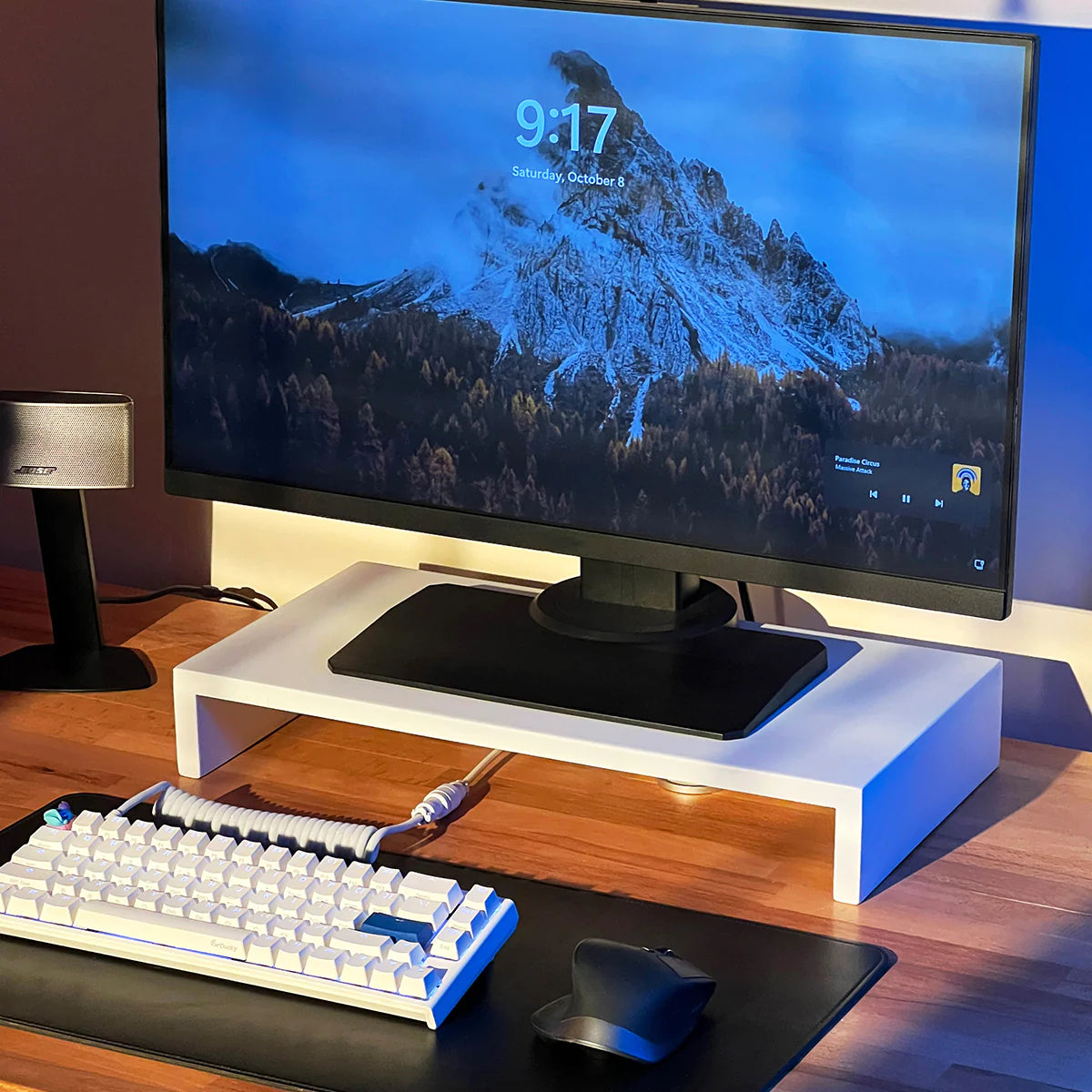 Modern stand riser by woodsy with a monitor displaying a mountain wallpaper, mechanical keyboard, mouse, and desk lamp.