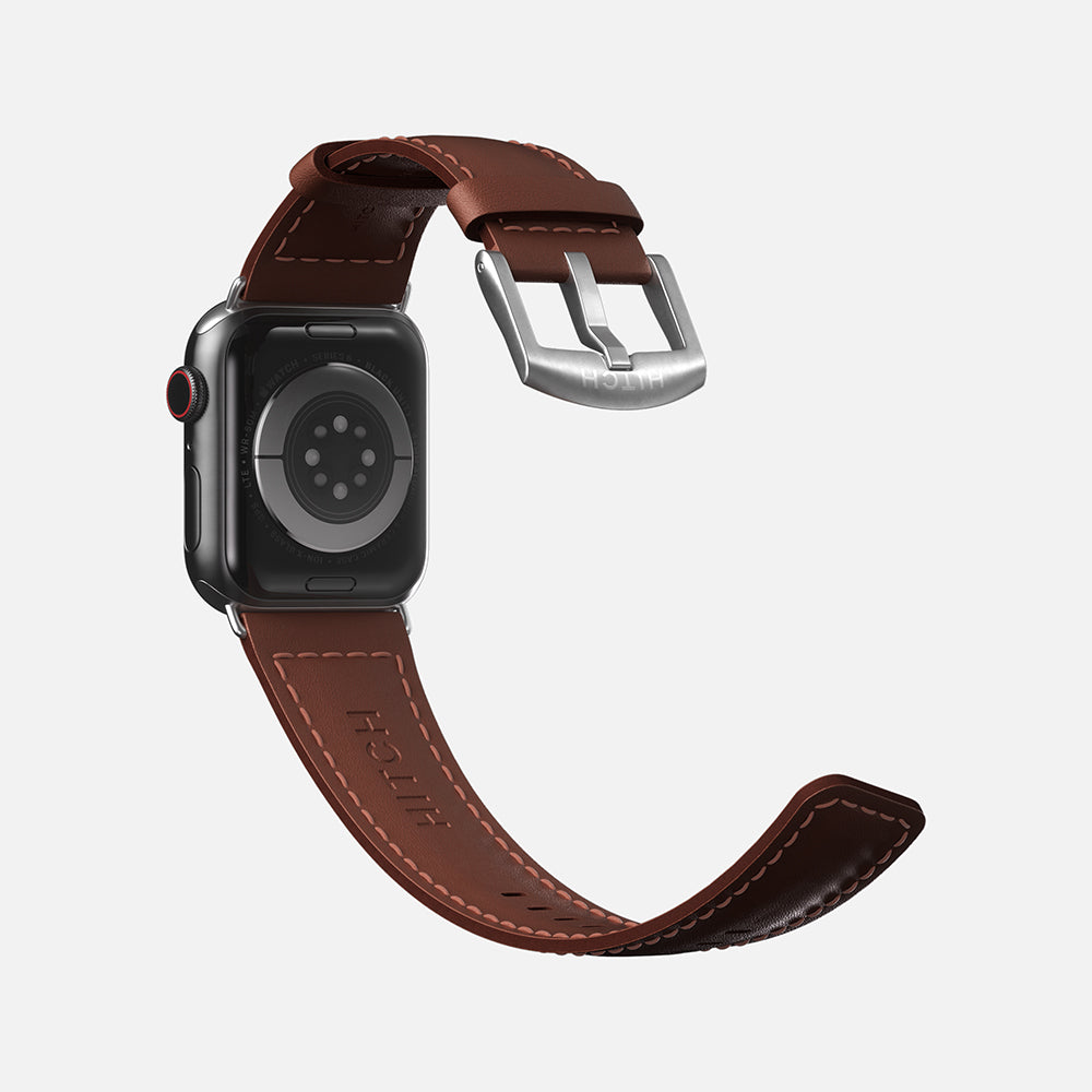 Apple Smartwatch with brown leather strap and silver buckle on white background.