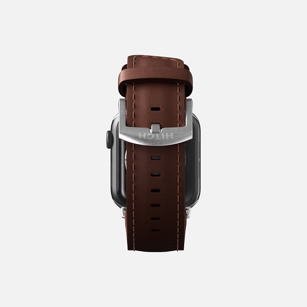 Rear view of a brown leather Apple smartwatch strap with silver buckle on a gray background.
