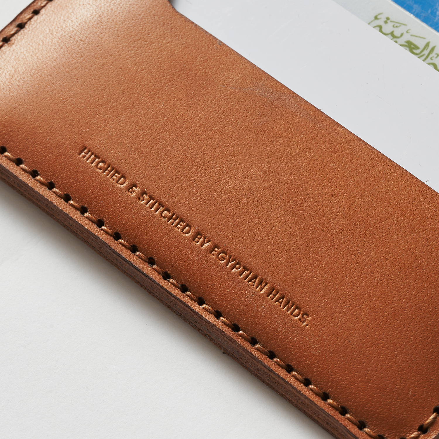 Close-up of a brown leather bifold wallet with embossed text and stitching, against a white background.